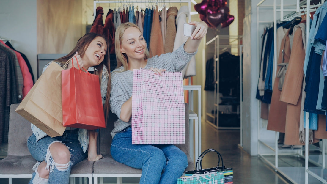 Two friends pose for a selfie with shopping bags.